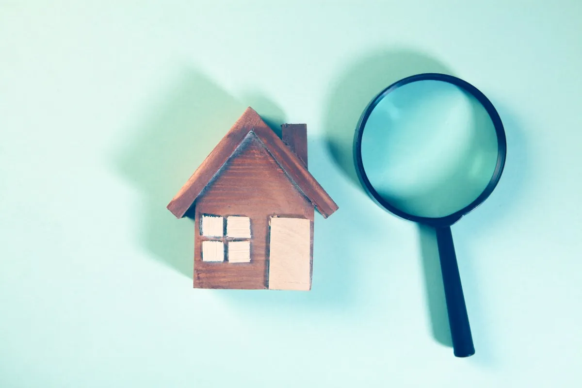 Magnifying glass inspecting a house model for title defects